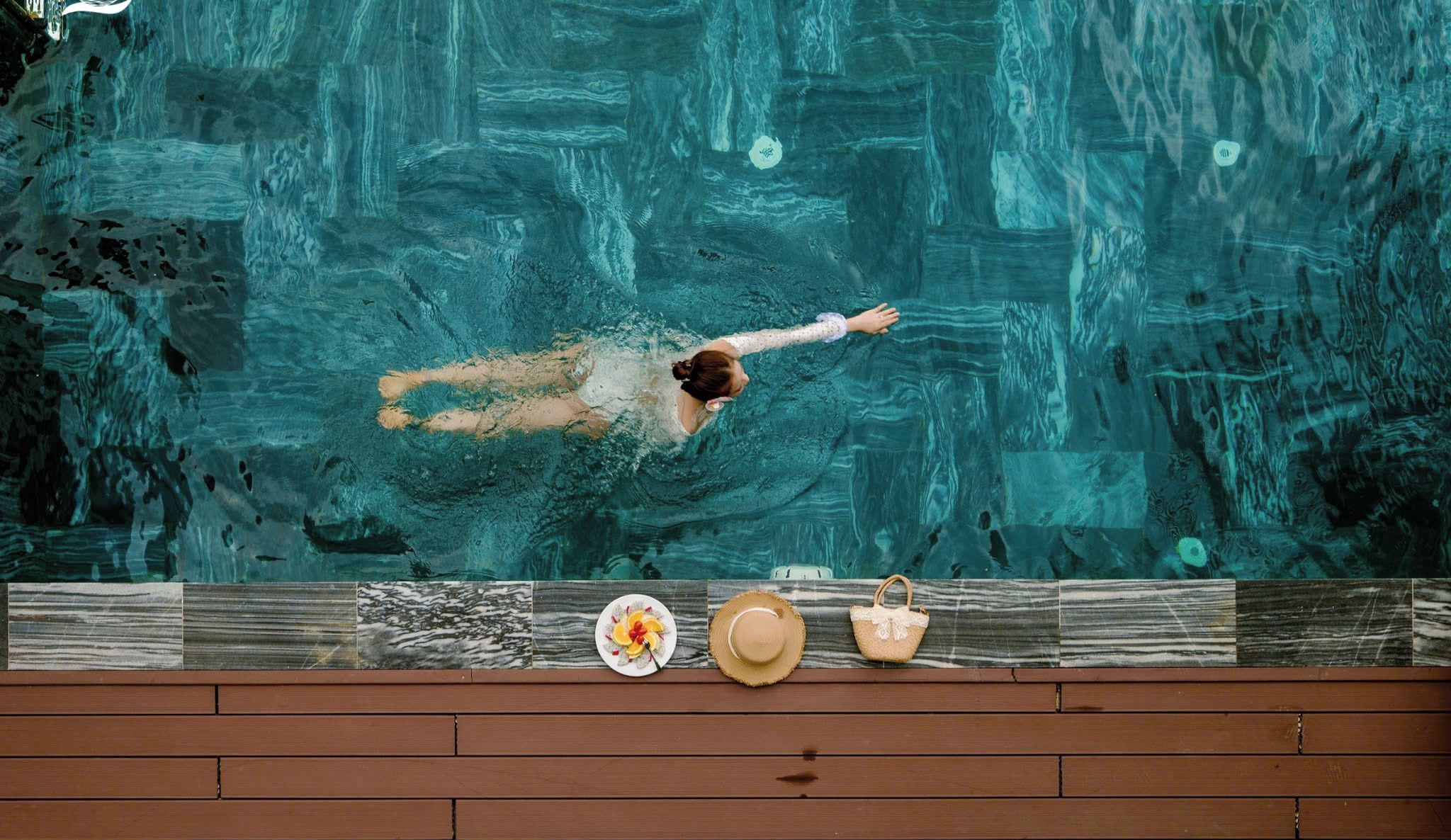 Una persona nada en una piscina con un muelle de madera al frente.