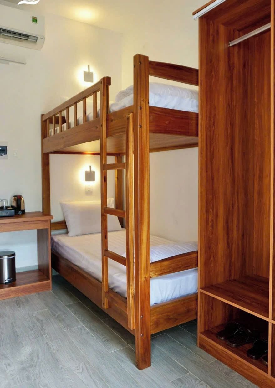 Une chambre avec un lit superposé, une armoire en bois et un bureau avec une poubelle.