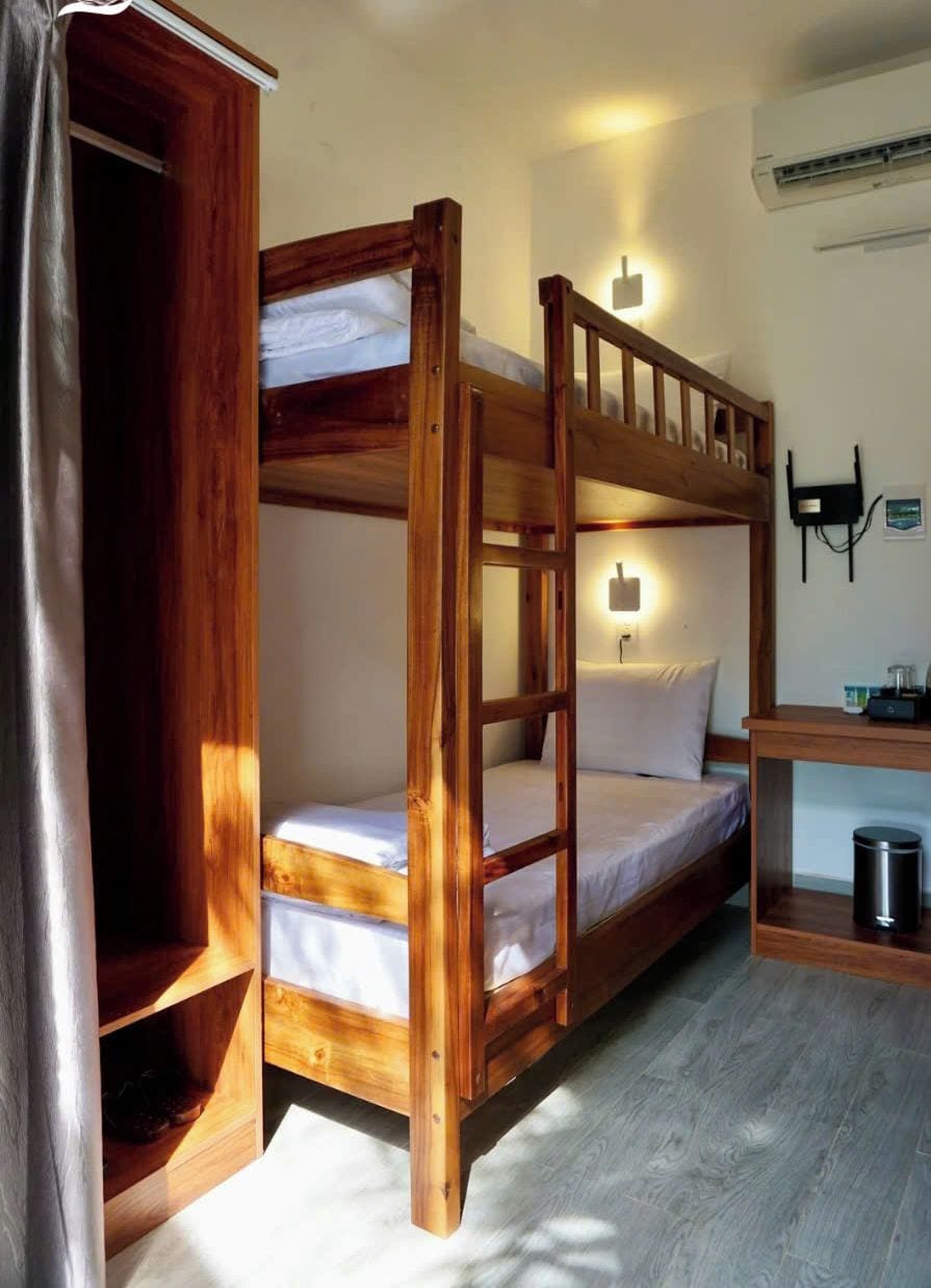 A bunk bed with a wooden frame, a bedside table, a lamp, and a trash bin.