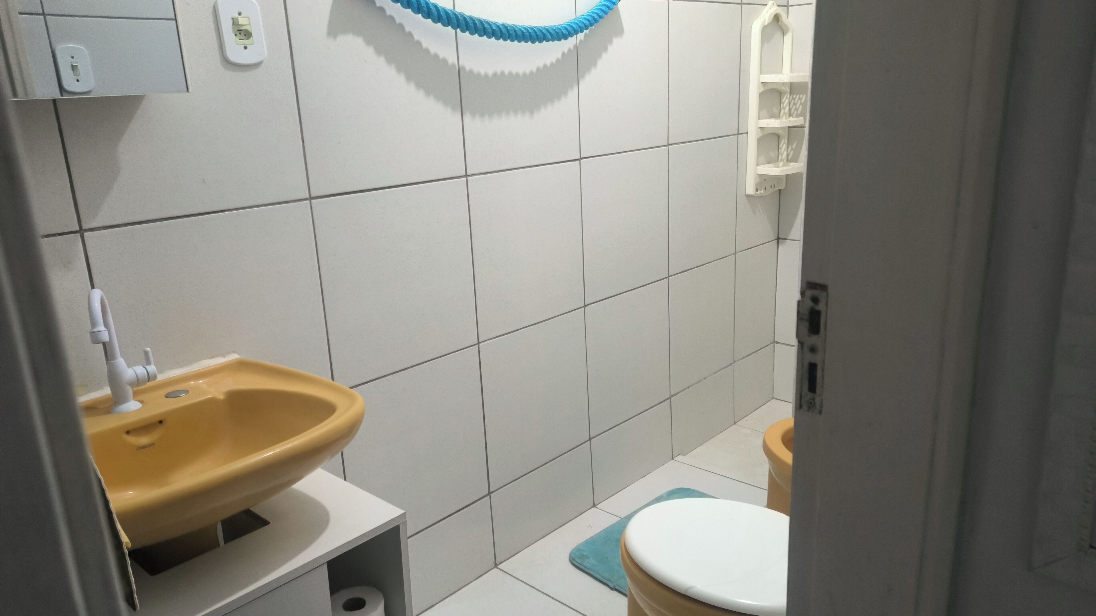 Un baño pequeño con un lavamanos amarillo, inodoro blanco y un tapete azul.