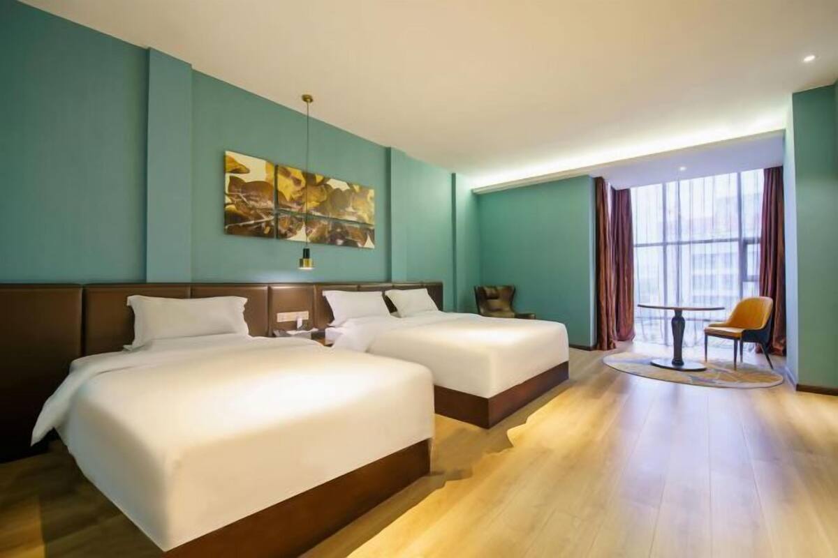 A hotel room with two beds, a large window with curtains, a round table, and a chair.