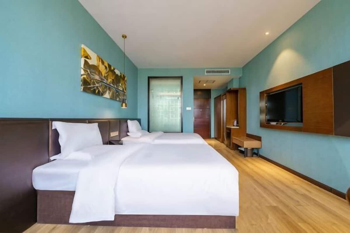 A hotel room with a large bed, a TV mounted on the wall, and a wooden floor.