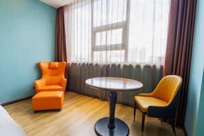 A room with a round table, two chairs, a bed, and a window with curtains.