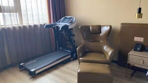 Una habitación con una cinta de correr, un sillón de cuero, un escritorio pequeño y una ventana con cortinas.