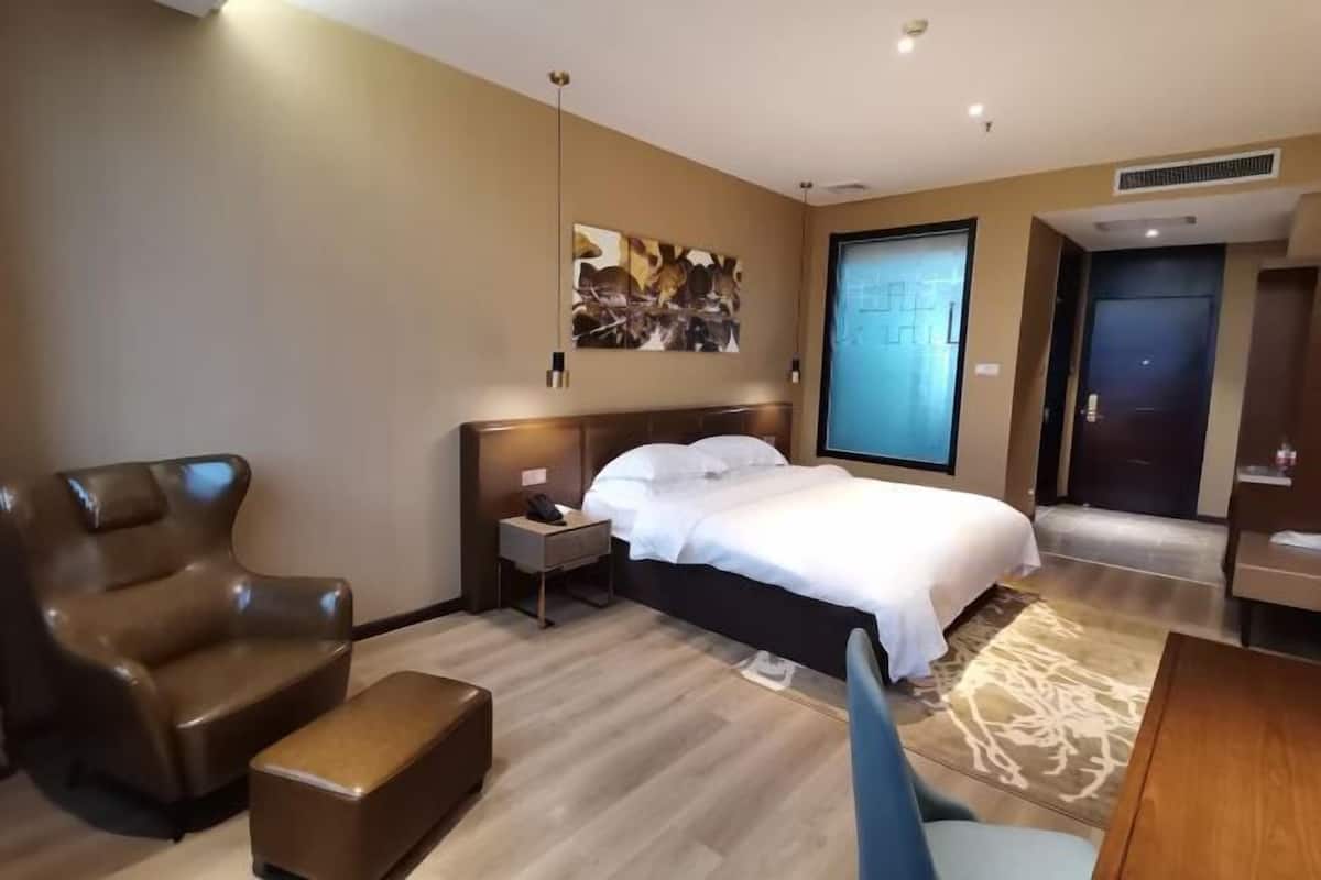 A hotel room with a bed, a chair, a nightstand, a desk, and a door.