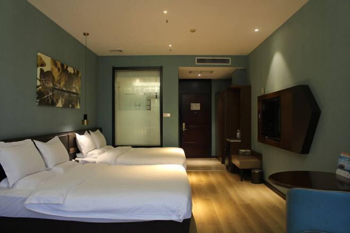 A hotel room with two beds, a TV, a desk, and a door leading to a bathroom.