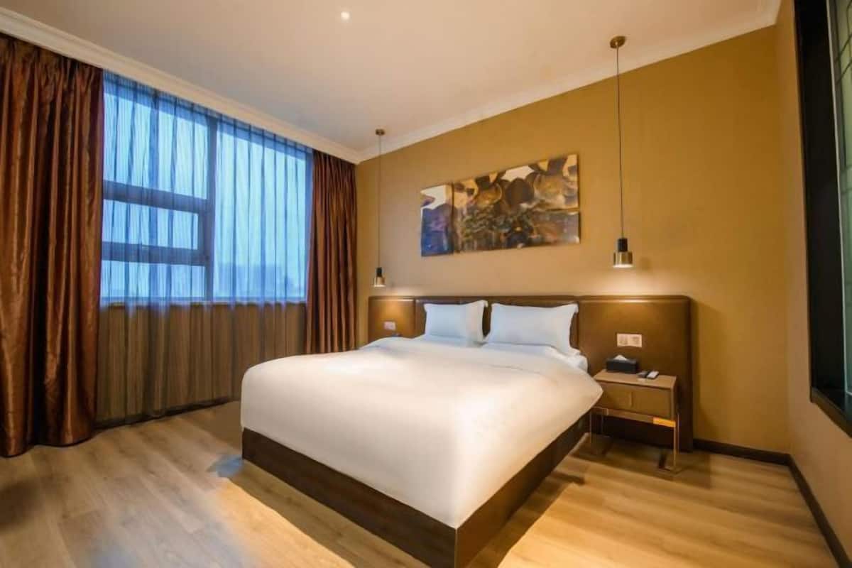 A hotel room with a large bed, a nightstand, a painting on the wall, and a window with curtains.