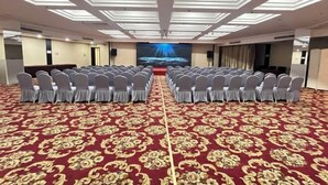 Un salón de conferencias con filas de sillas, una pantalla grande al frente y una alfombra estampada.