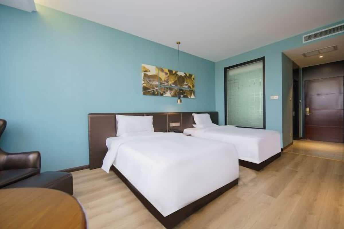 A hotel room with two beds, a sofa, a painting on the wall, and a door.
