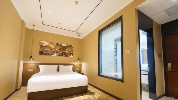 Habitación de hotel con una cama grande, una ventana, un cuadro en la pared y una puerta que da a otra habitación.