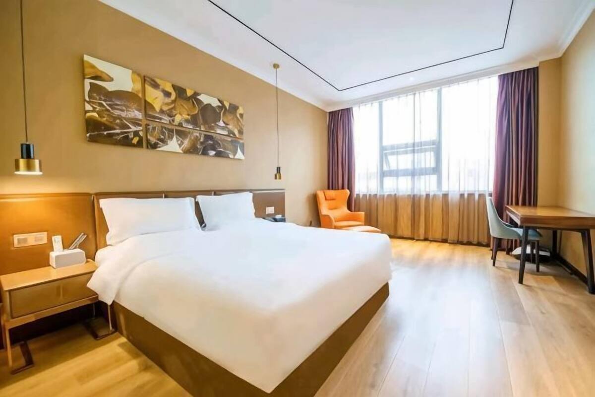 A hotel room with a large bed, a desk, a chair, and a window with curtains.