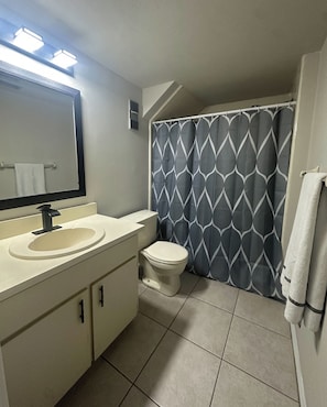 A bathroom with a sink, mirror, toilet, and shower curtain.
