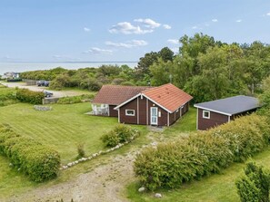 Une maison en bois à deux étages, avec un toit rouge, une terrasse couverte et une vue sur la mer.