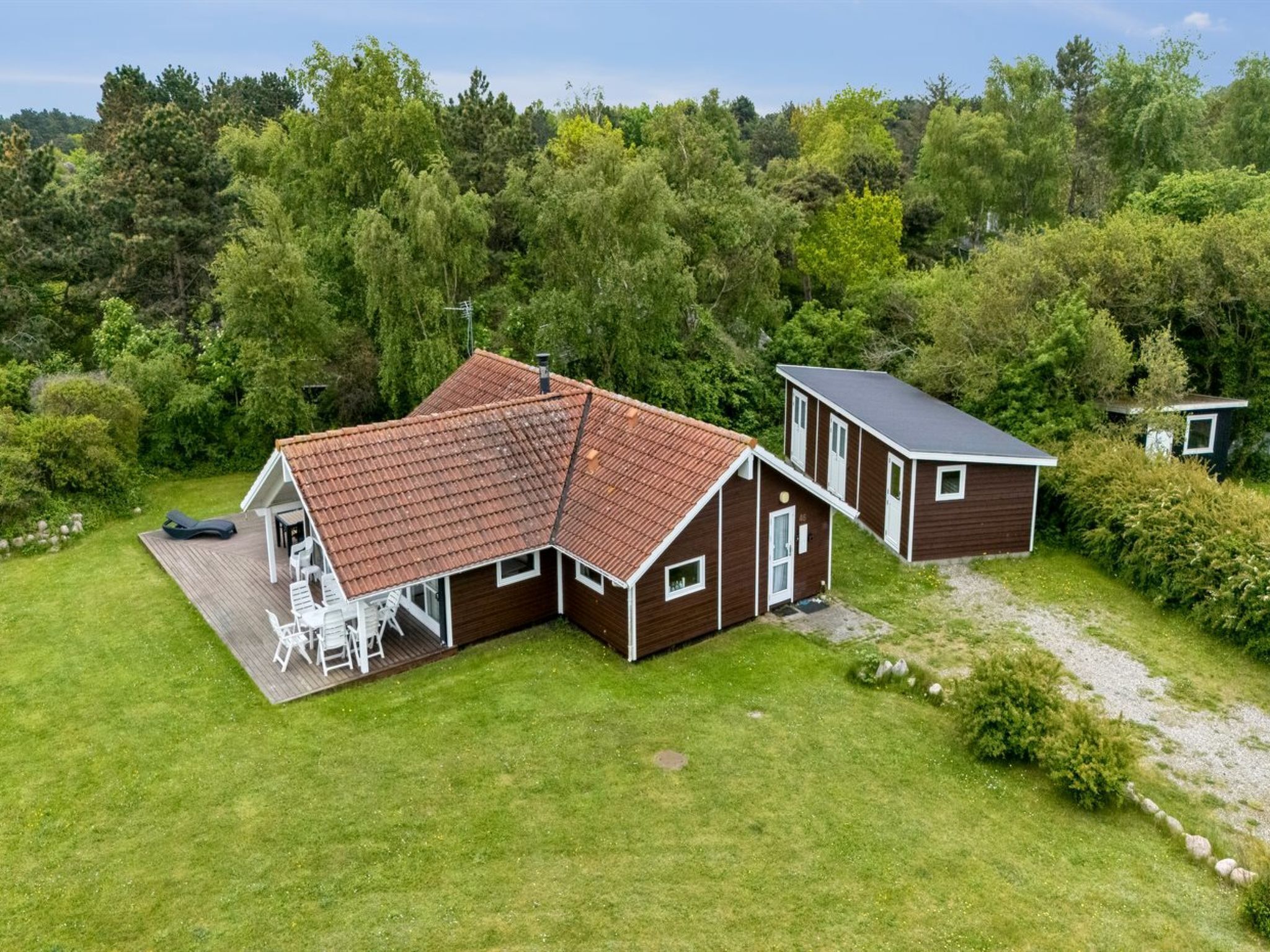A two-story house with a red-tiled roof, a deck with chairs, and a small shed.