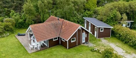A two-story house with a red-tiled roof, a deck with chairs, and a small shed.