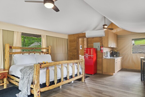 A wooden-framed bed with a headboard, a red refrigerator, and a kitchen area with wooden cabinets. - Luxury Primitive Camping + Private Zoo Access (Troutman)