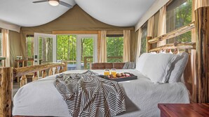Ruime slaapkamer met een groot bed, een houten hoofdbord, een plafondventilator en uitzicht op de omgeving.