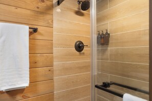 A wooden-paneled bathroom with a glass shower enclosure, a towel rack, and a soap dispenser. - Luxury Primitive Camping + Private Zoo Access (Troutman)