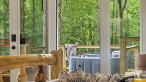 Een kamer met een groot raam, een tafel met een tafelkleed en een stoel.