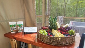 Een rieten mand met fruit op een houten tafel, met twee kopjes en een bordje welkomstbericht.