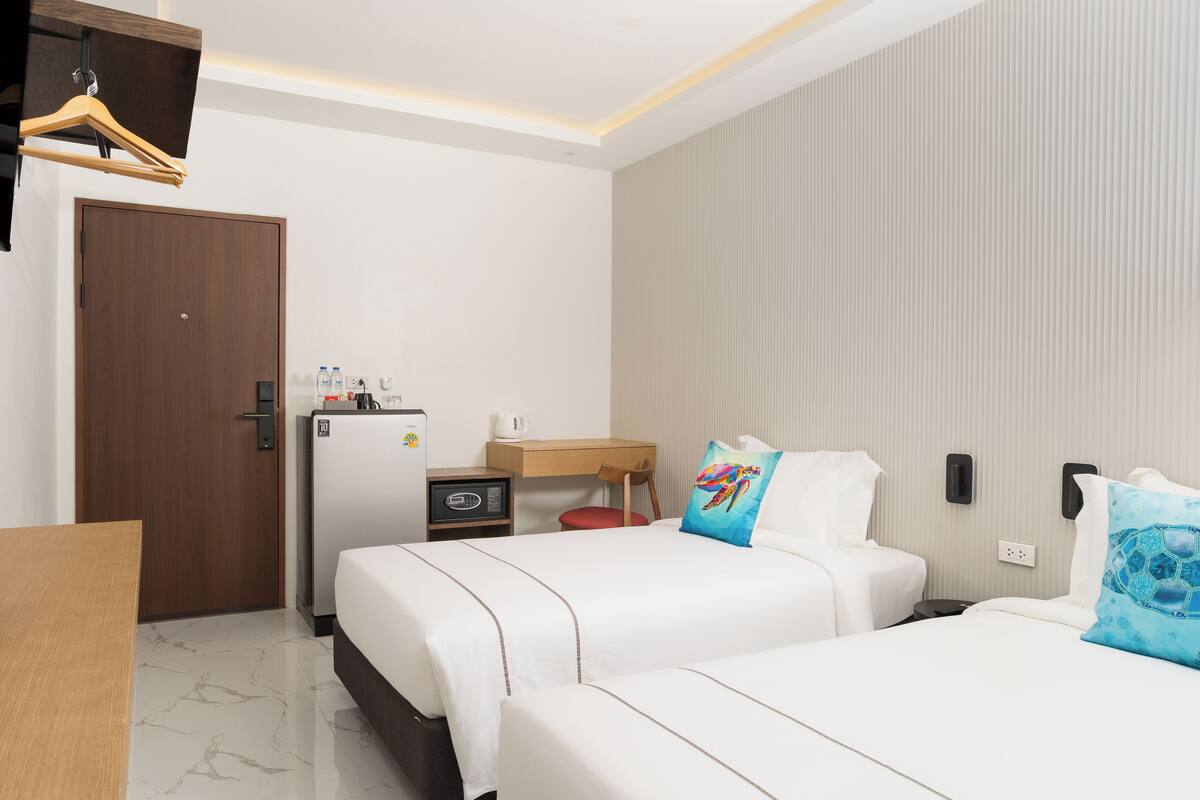 Una habitación de hotel con dos camas, un escritorio, un refrigerador y un armario de madera.