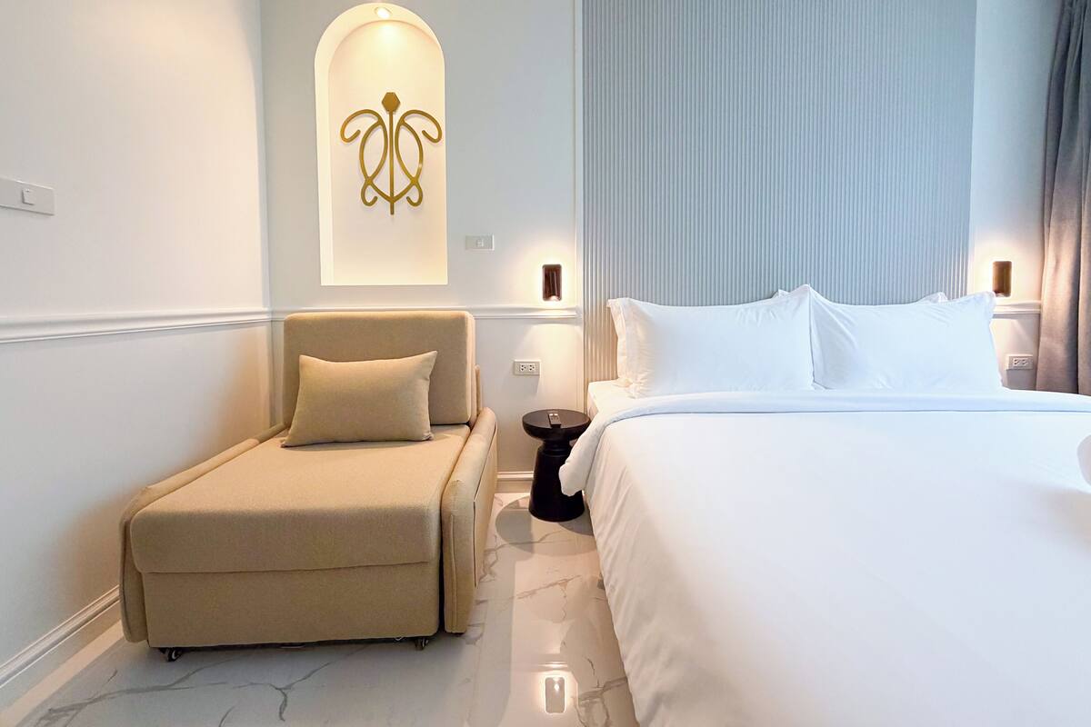 Una habitación de hotel moderna con cama, sofá, lámpara de pared y ventana con cortinas.