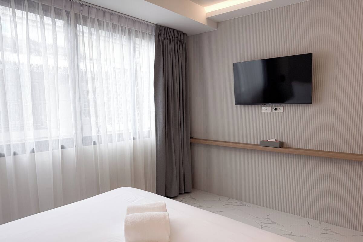 Una habitación de hotel moderna con una cama grande, un televisor de pantalla plana en la pared y cortinas translúcidas en la ventana.