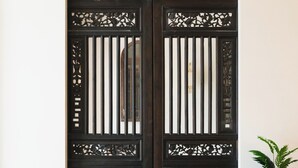 Una puerta de madera tradicional con tallas intrincadas, un suelo de baldosas oscuras, un tapete estampado, una silla de madera y una planta en maceta.