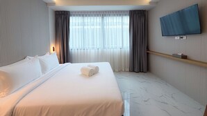 Habitación de hotel con una cama grande, un televisor de pantalla plana en la pared y una ventana con cortinas.
