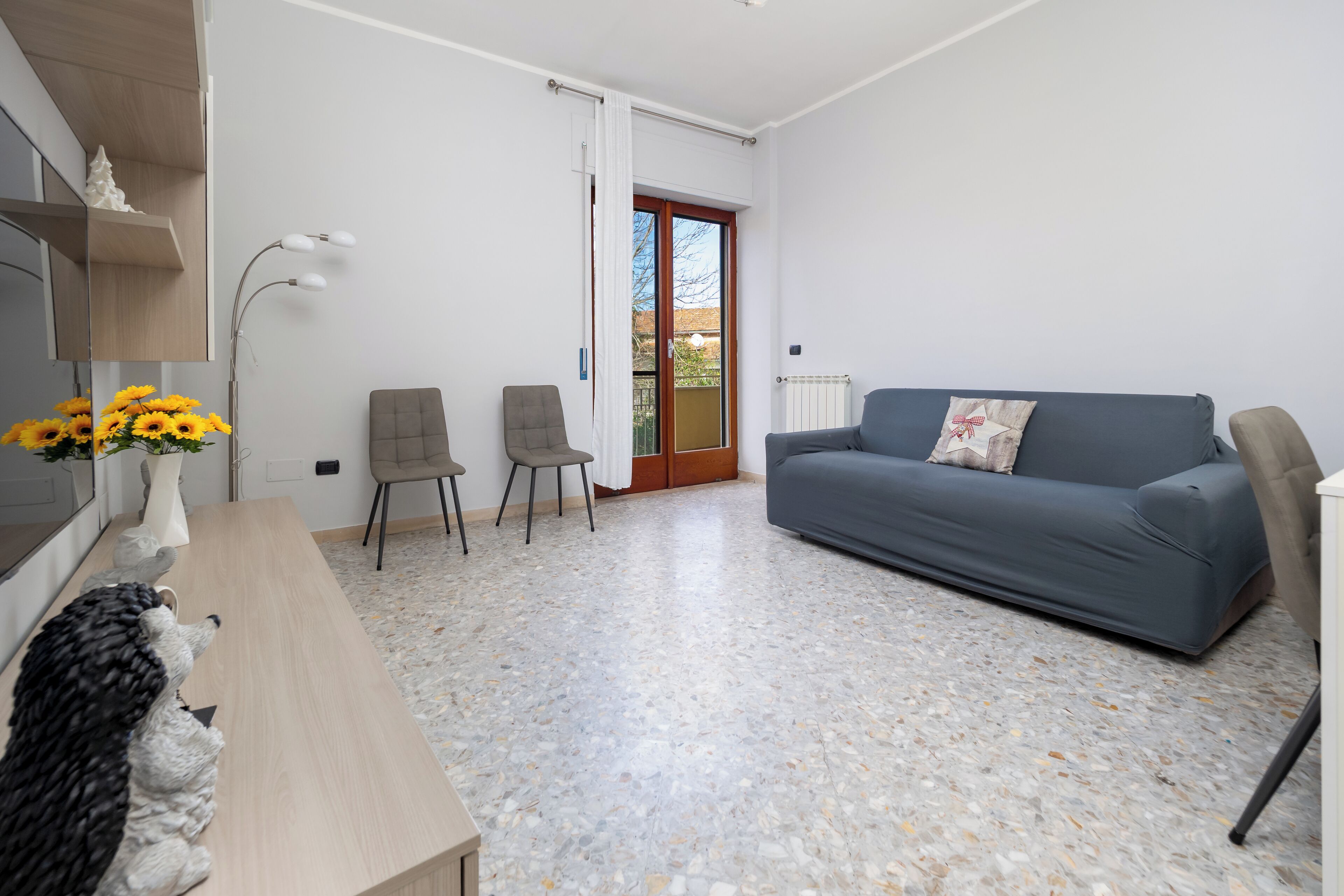 A modern living room with a grey sofa, two chairs, a wooden coffee table, and a vase with sunflowers.