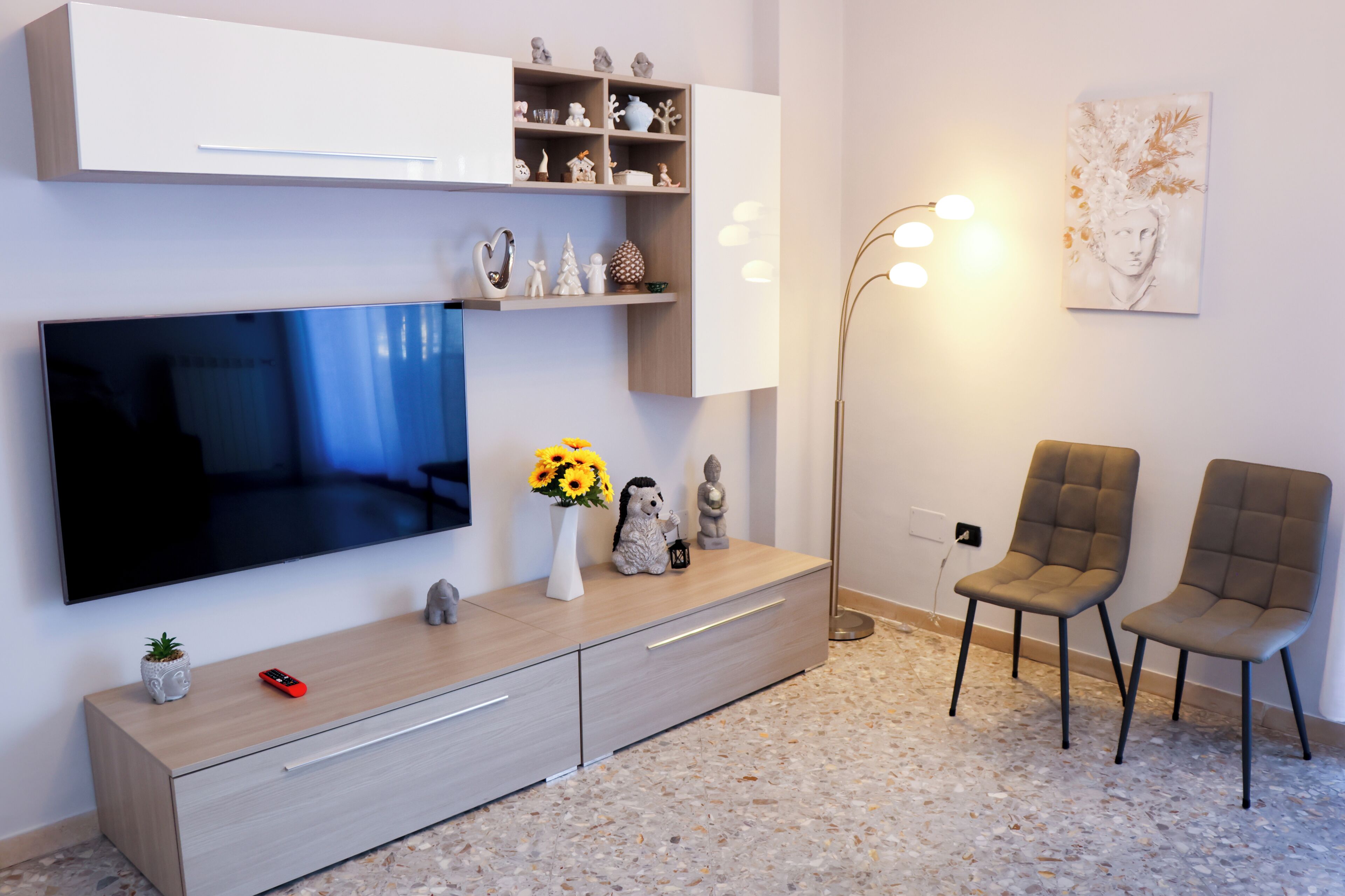 A modern living room with a flat-screen TV, a wooden cabinet, a floor lamp, and two upholstered chairs.