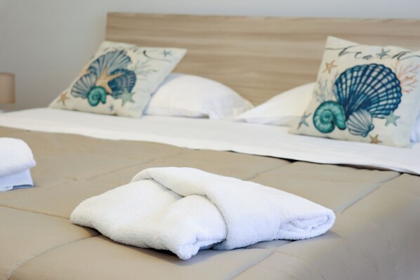 A neatly made bed with white linens and two decorative pillows with a shell design.