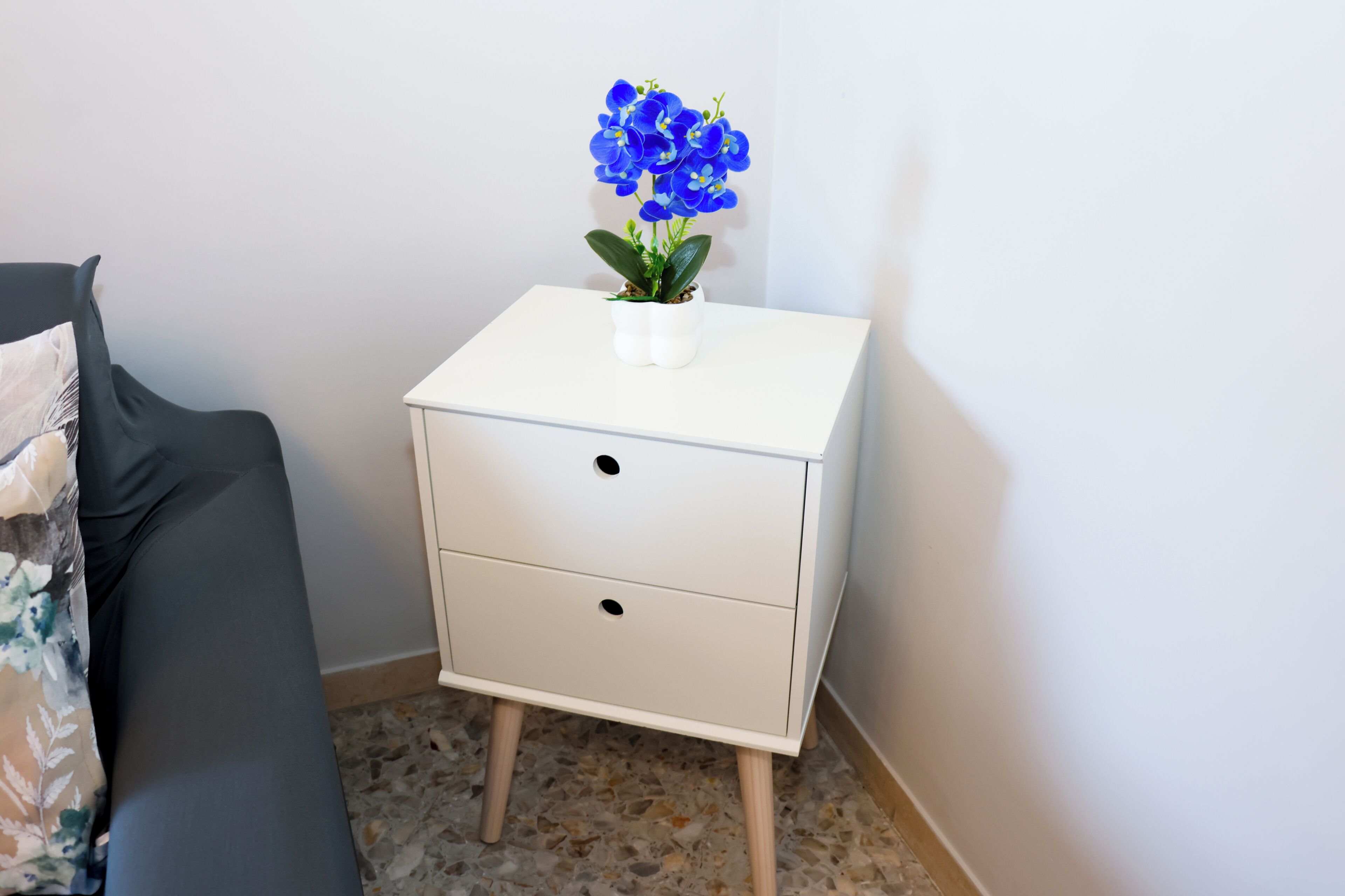 A white bedside table with two drawers and a small potted orchid.