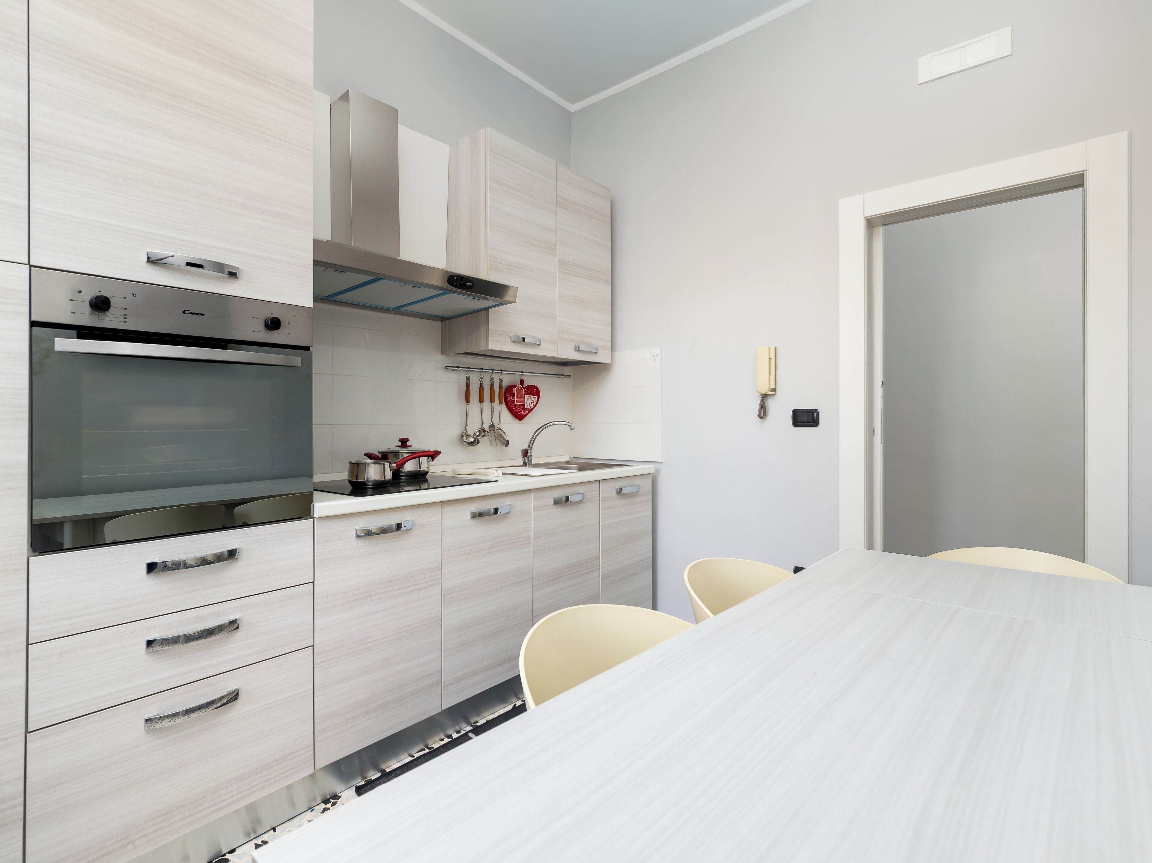 Une cuisine moderne équipée d’un four encastré, d’une cuisinière et d’un évier. On y trouve des placards, un plan de travail et une table à manger avec des chaises.
