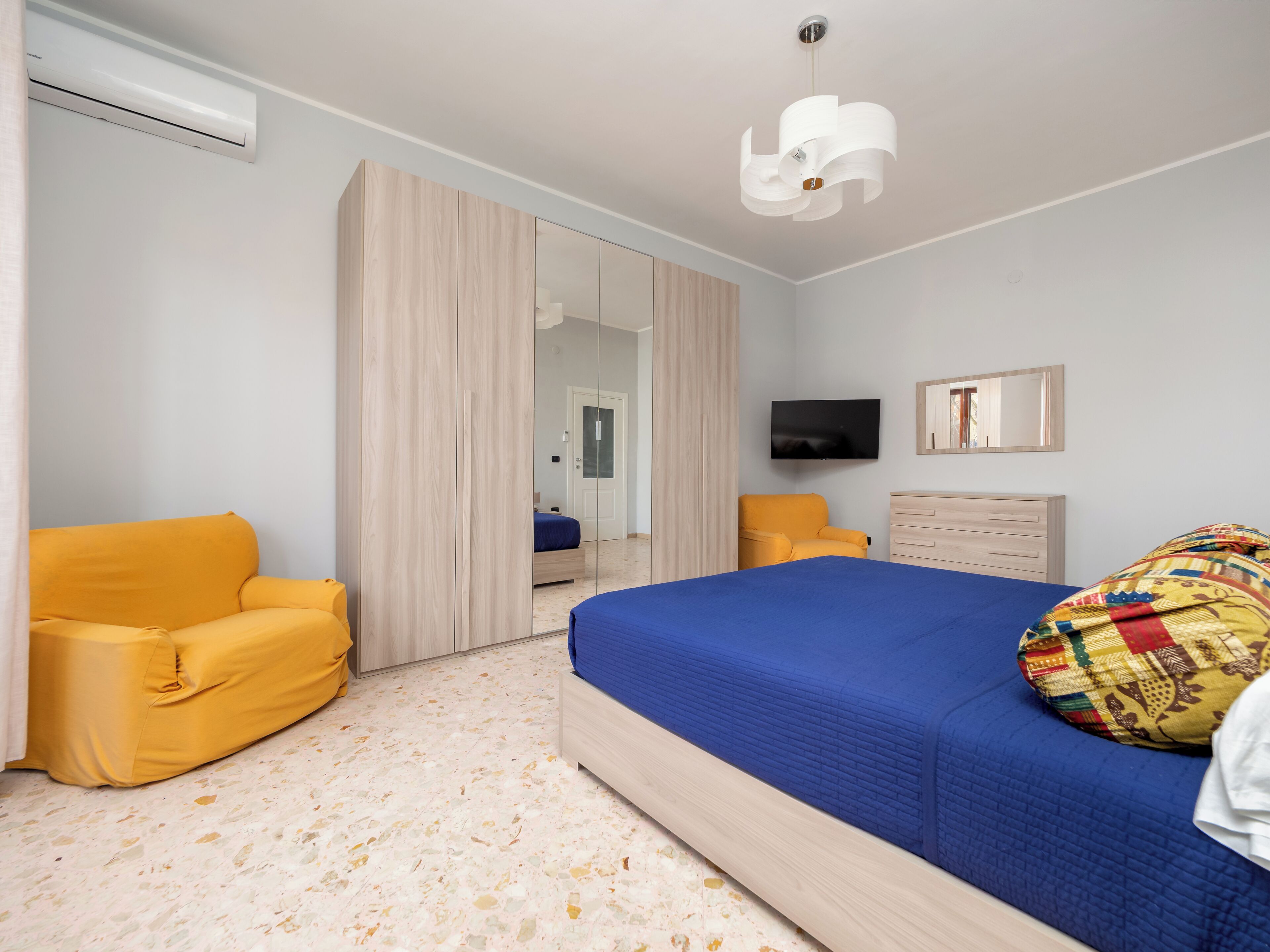 A bedroom with a bed, a wardrobe, a television, and a chair.
