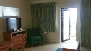 A living room with a television, a green armchair, a ceiling fan, and a sliding glass door leading to a balcony. - Pompano Beach FL - Oceanfront Condos ~ 1 Bdrm $1399/Week, Studio $995/Week (Pompano Beach)