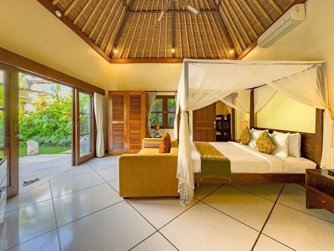 A spacious bedroom with a canopy bed, a sofa, and a view of greenery outside.