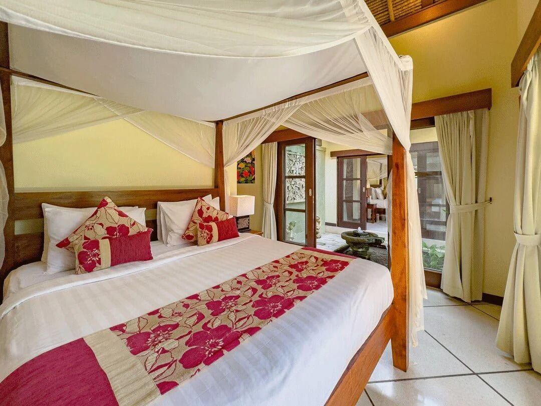 A bedroom with a canopy bed, a view of the outside, and a window with curtains.