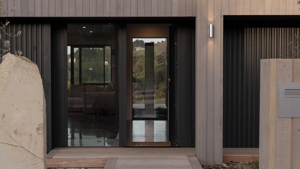 A modern building entrance with a glass door, wooden steps, and a metal gate. - Studio Āio - Raglan Retreat With Sauna (Raglan)