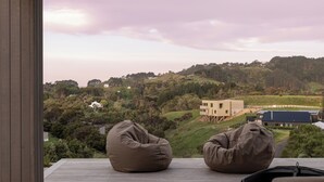 A deck with two bean bags and a grill, overlooking a hilly landscape with buildings. - Studio Āio - Raglan Retreat With Sauna (Raglan)