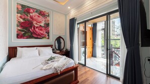 A bedroom with a large floral painting, a wooden bed, a mirror, and a view of the outside balcony. - Ben Thanh Maison (Ho Chi Minh City)