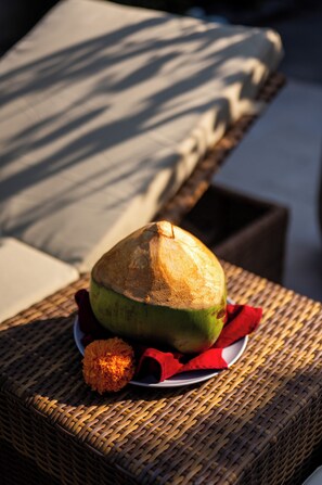 A woven chair with a cushion, a plate with a coconut and a flower, and a red napkin. - Island Getaway Villa (Denpasar)