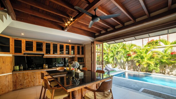 A spacious kitchen with wooden cabinets and a dining area with a glass table. - Island Getaway Villa (Denpasar)