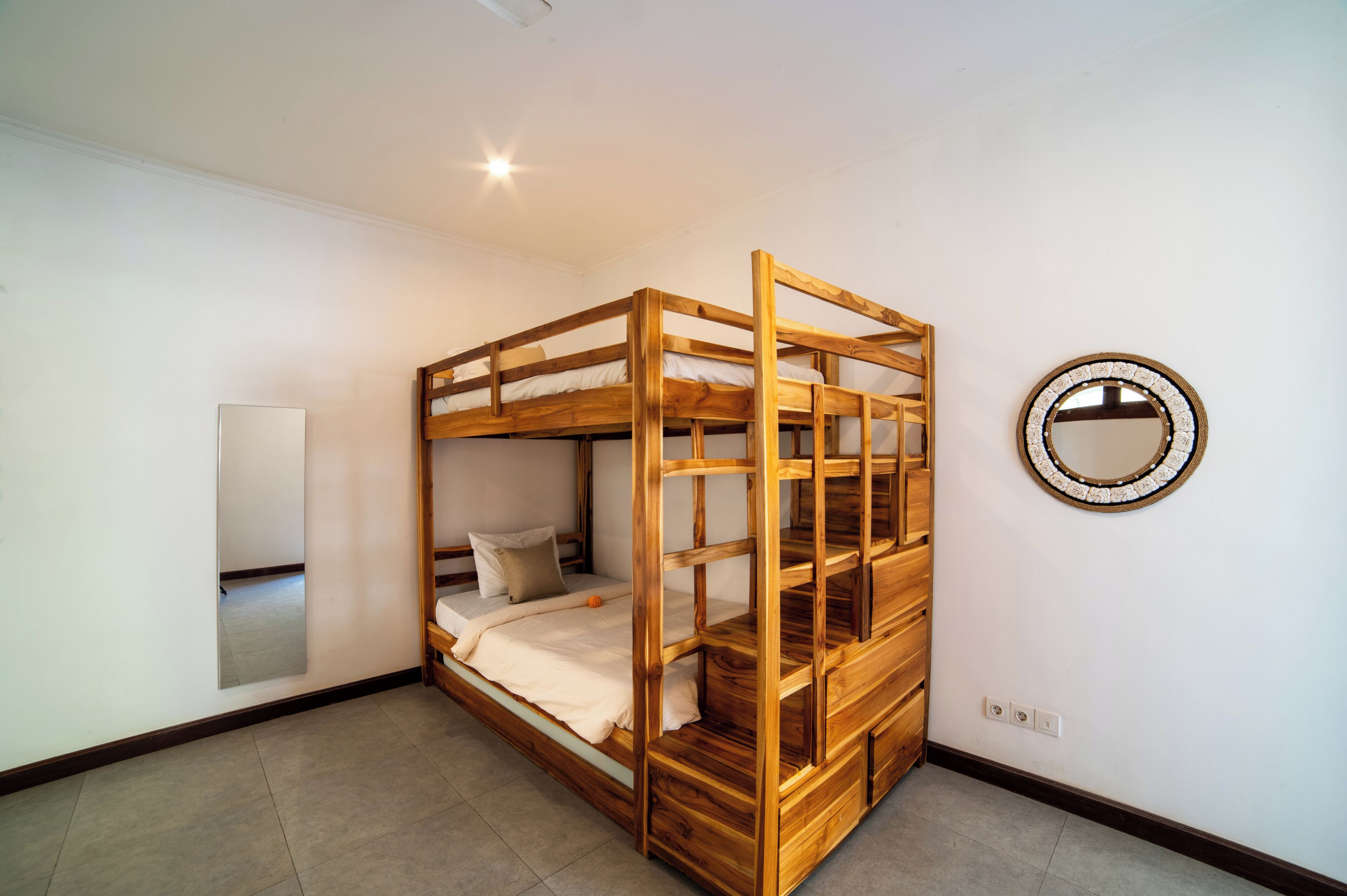 Una cama litera con estructura de madera, un espejo en la pared y suelo de baldosas.