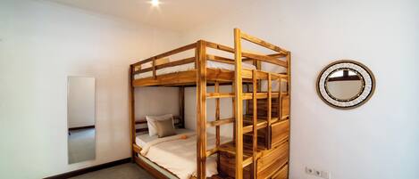Una cama litera con estructura de madera, un espejo en la pared y suelo de baldosas.