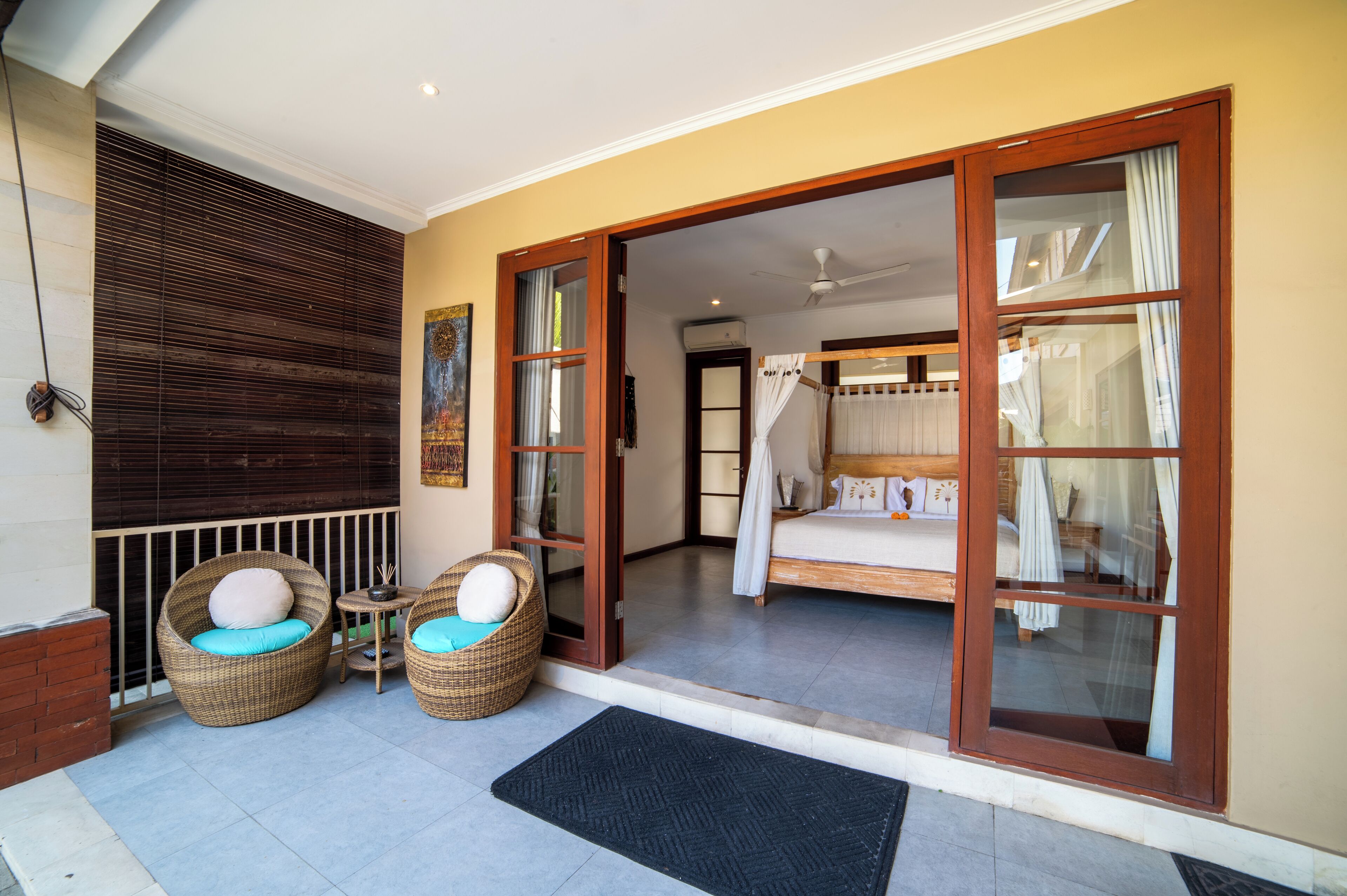 A room with a bed, a window with curtains, and wicker chairs with cushions.