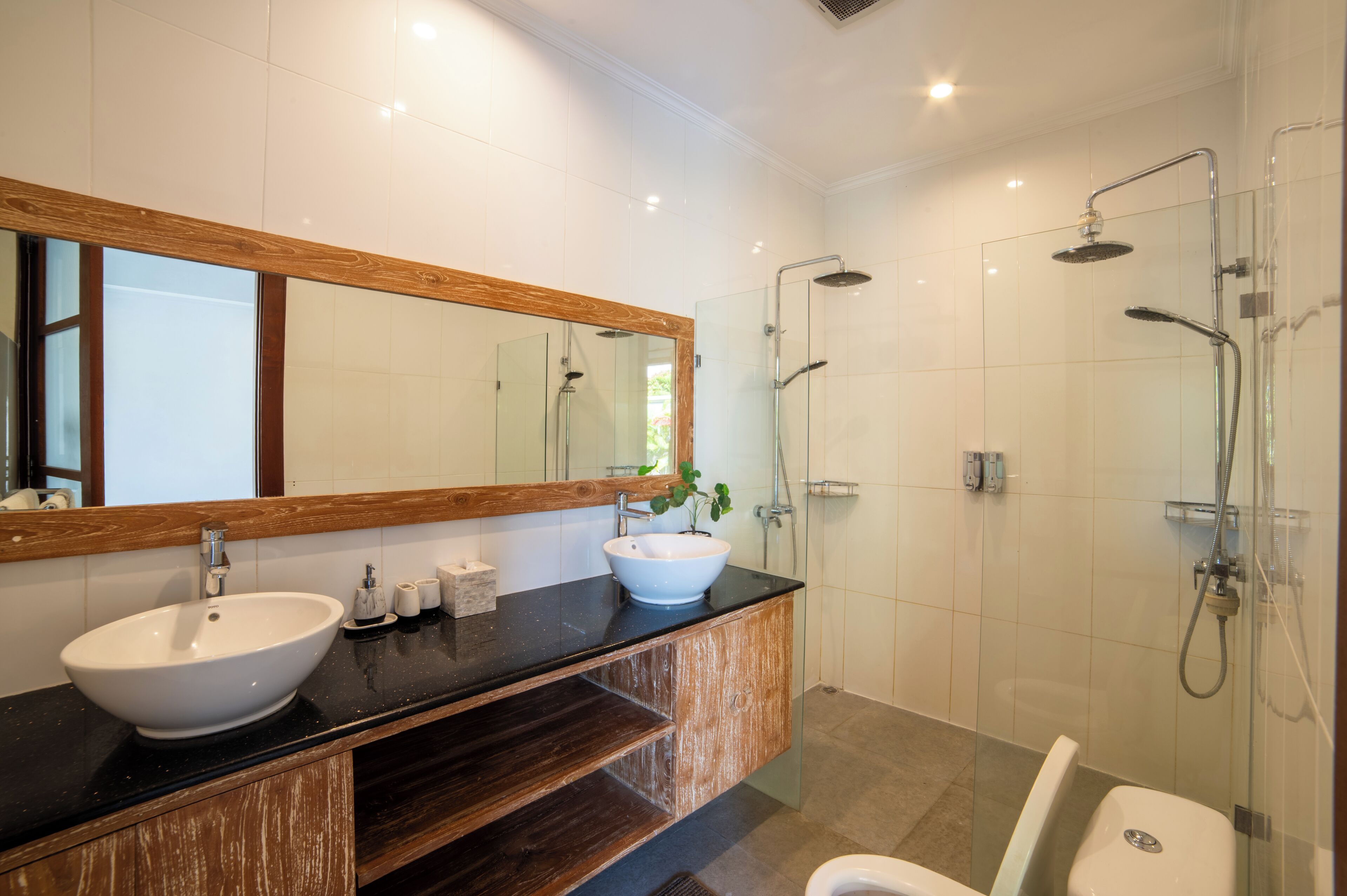 A modern bathroom with a large mirror, two sinks, a shower area, and a toilet.