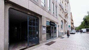 A building with a barbershop on the ground floor, a tiled sidewalk, and a few pedestrians in the distance.