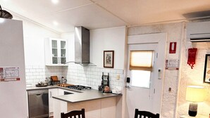 Een compacte keuken met witte kastjes, een centraal eiland en een eethoek met een houten tafel en stoelen.