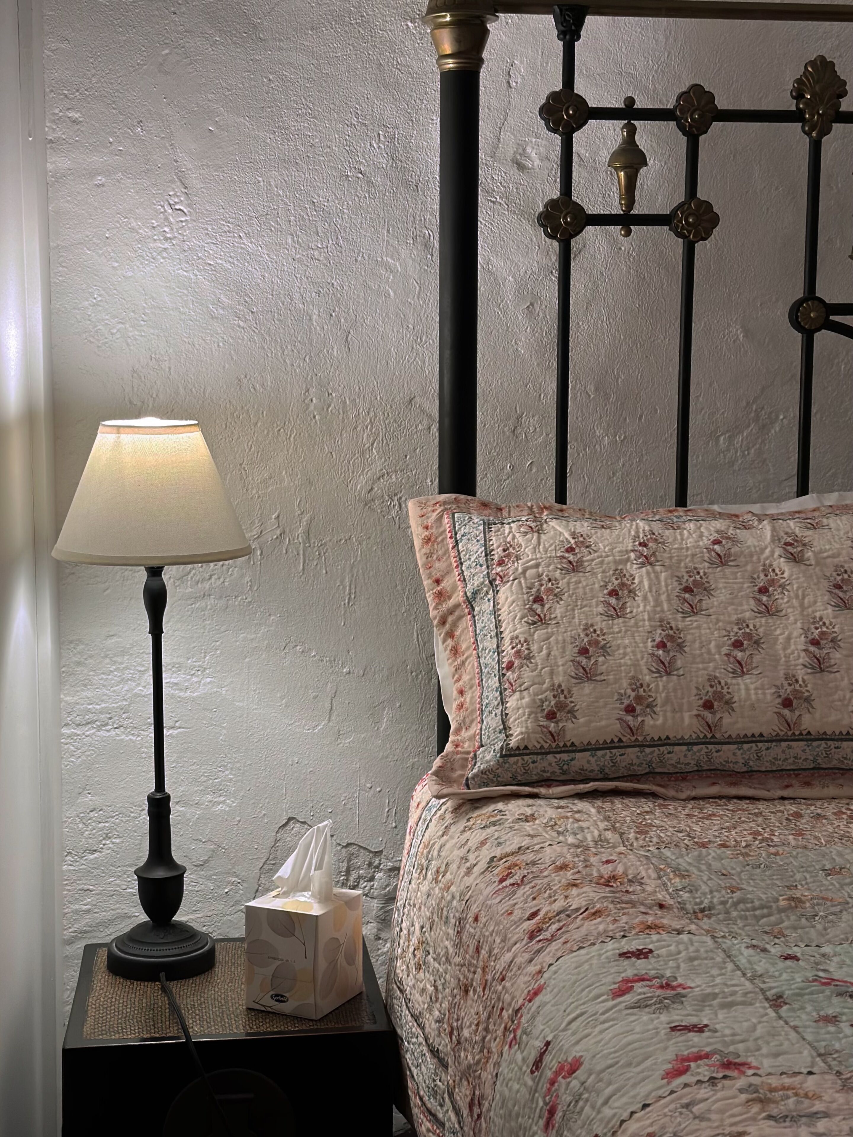 A bed with floral bedding, a bedside lamp, and a tissue box on a nightstand.